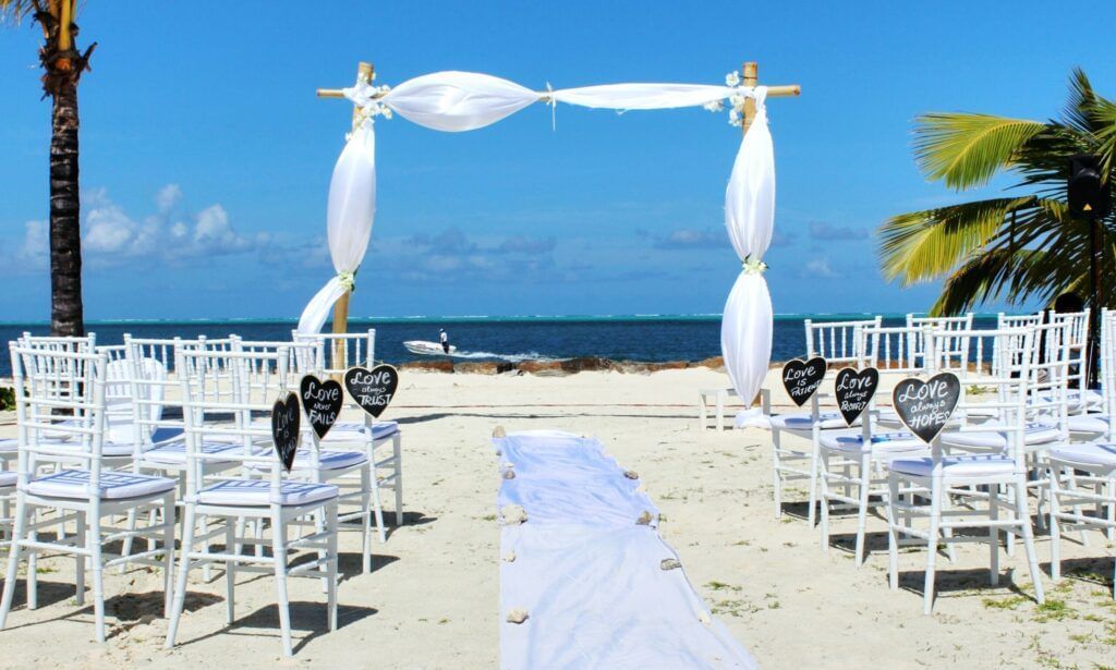 Beach wedding setup with white chairs and a floral archway.