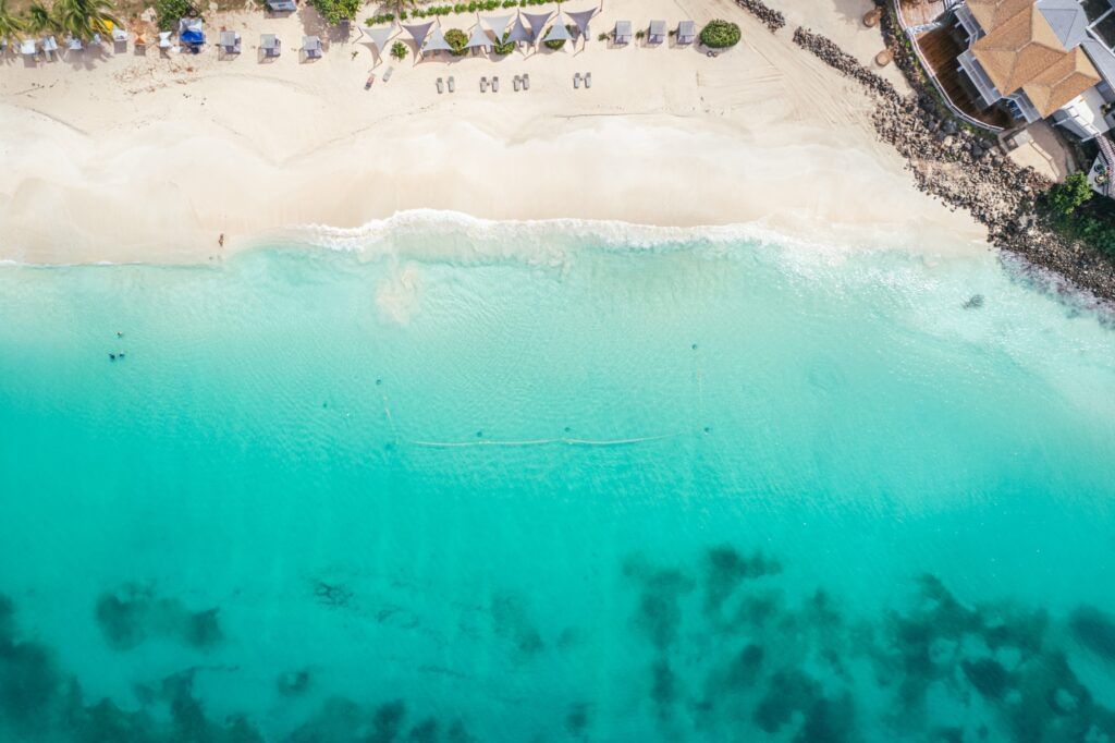 An overhead shot of a stunning white sand beach curving into a clear, bright turquoise ocean with gentle waves.