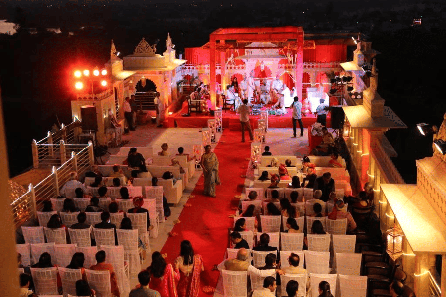 A traditional Indian wedding ceremony on the long terrace, showing guests seated in rows facing a grand, brightly lit mandap structure at Chunda Palace, Udaipur.