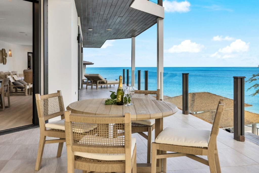 An outdoor dining area with a wooden table and chairs on a balcony overlooking the ocean.