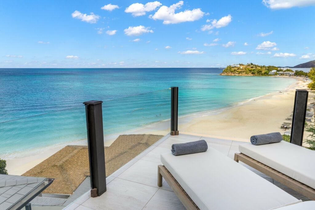 A serene beach scene with lounge chairs under umbrellas on a wooden deck extending over calm, clear blue water.