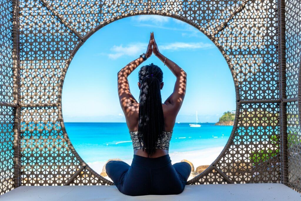 A silhouette of a woman sitting with her arms held above her head in a praying manner, facing the sea.