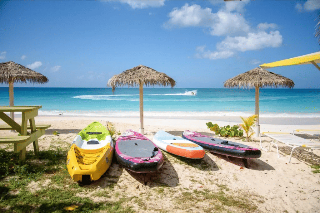Colorful kayaks and paddleboards on a white sand beach with thatched umbrellas and turquoise water.