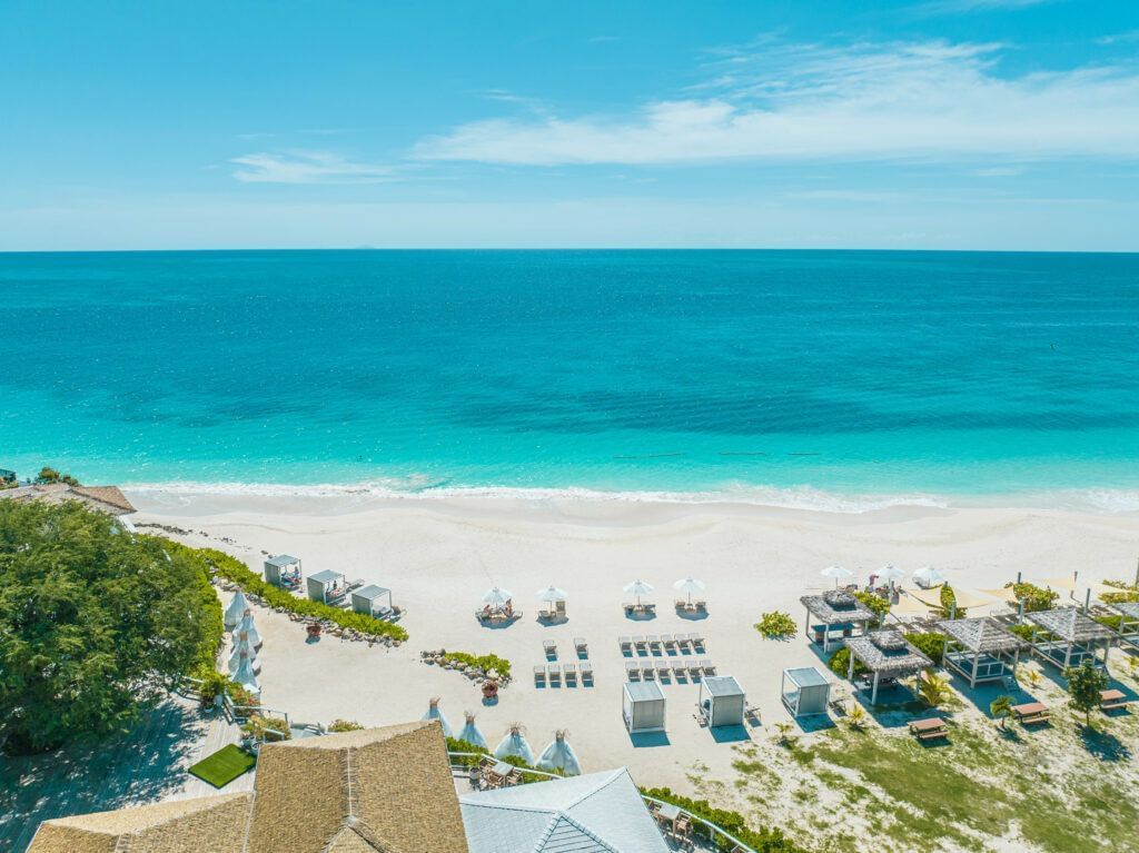 Aerial view of a white sand beach and turquoise sea with sun loungers and umbrellas at Tamarind Hills Resort and Villas - Antigua.