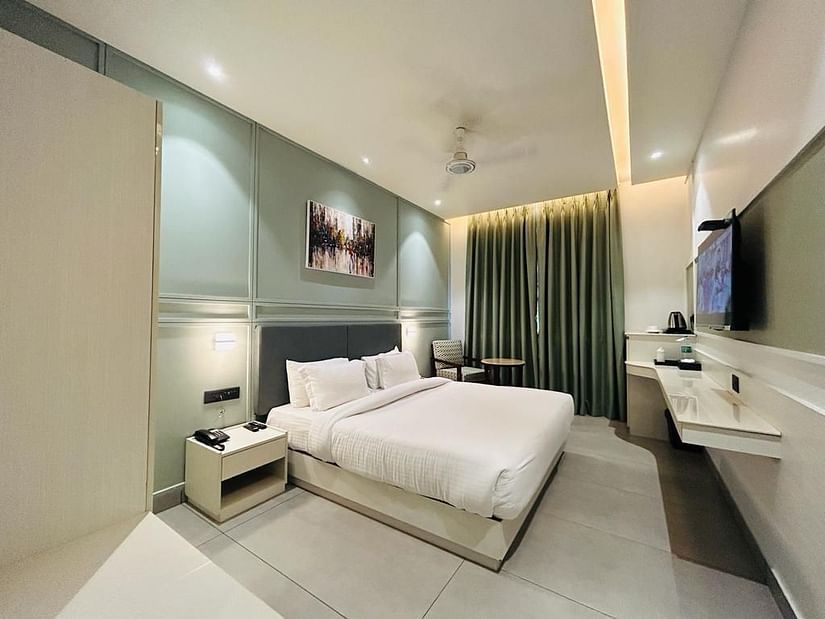 A well-arranged room with a tidy bed, wall art, a television, a tea & coffee maker and a comfortable sofa chair - Five Elements Hotels Goldleaf, Haldwani