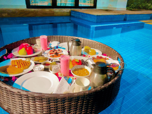 A huge basket containing several food items in it floating on the outdoor swimming pool.