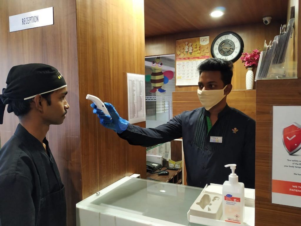 Staff checking temperature of another staff member at the entrance.