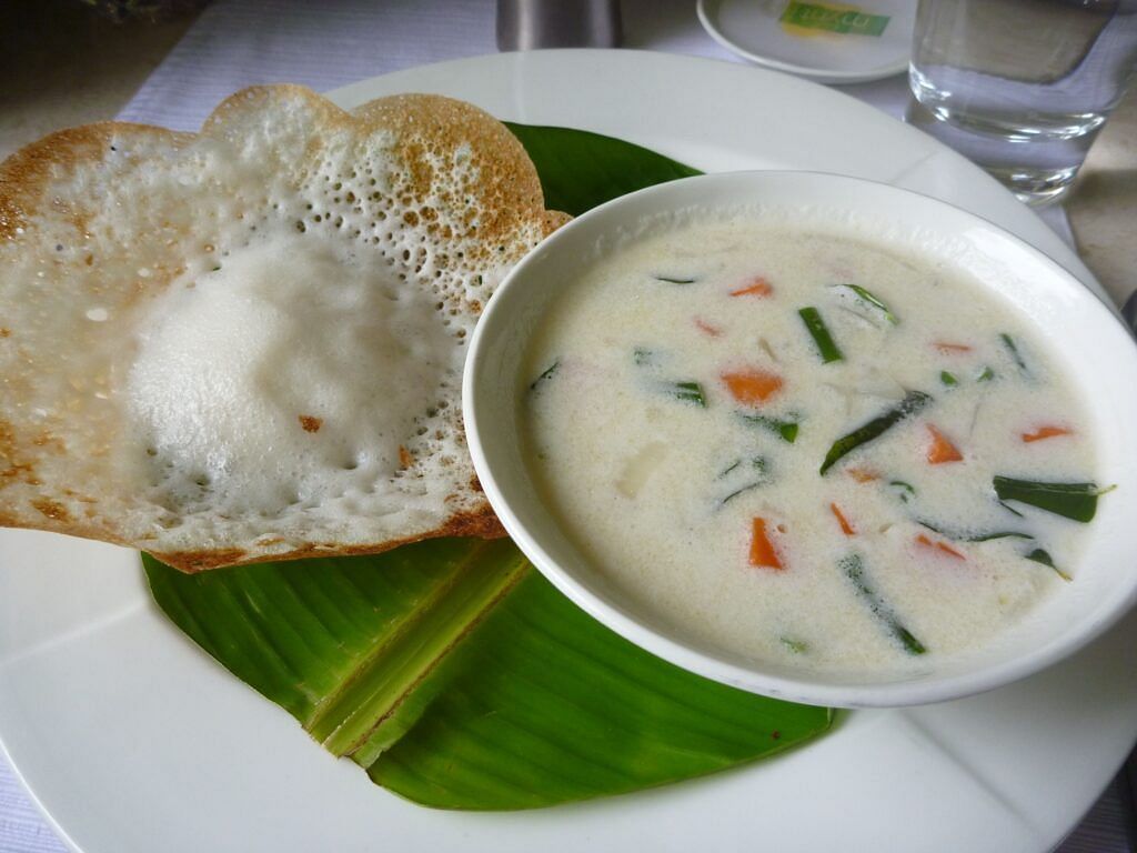 Appam served with a bowl of coconut vegetable stew on a banana leaf.