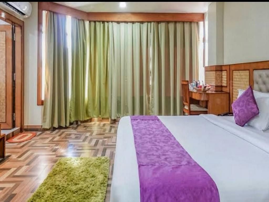 A spacious bedroom with rich wooden flooring, green drapes, and a purple-accented bed for a cosy stay - Pemaling Lords Eco Inn Guwahati