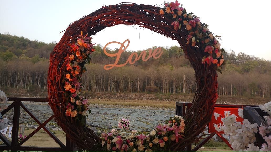 An image of a well decorated stage with wooden twigs, dried grass and flowers behind it there is a river and a steep mountain