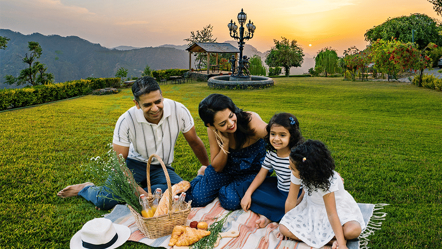 A family of four enjoying in open garden. It is a promotional banner offering 20% discount on morning yoga session, 105 discount, and more at The Manor Sports & Wellness Hotel.
