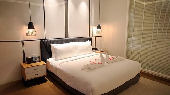 Image featuring a warm-lit room with a plush bed on which towels are made into two swans