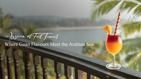 A promotional banner for Azzurra at Fort Tiracol featuring a tropical cocktail with the Arabian Sea and palm trees in the background.