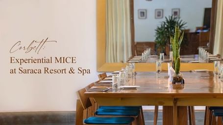 Elegant dining setup indoors with long wooden table and yellow accents, text overlay: Corbett: Experiential MICE at Saraca Resort & Spa.