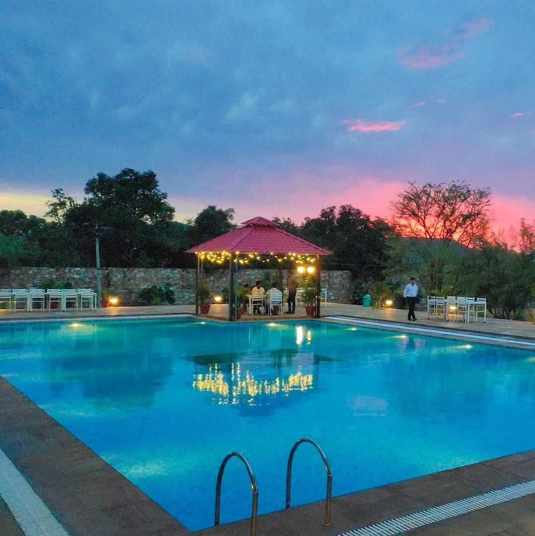 An outdoor swimming pool at dusk with a pink and blue sky in the background - Bamboo Saa Mulberry Resort, Pushkar