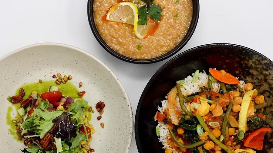Top-down view of three dishes, including a salad with nuts, a lentil soup with lemon, and a stir-fried vegetable dish with rice.