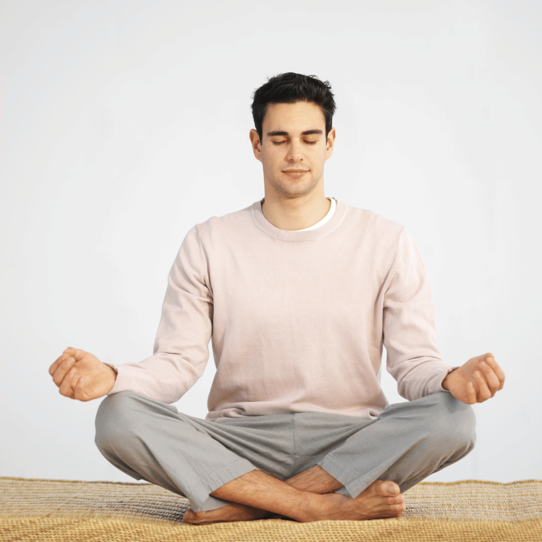 Man sitting cross-legged and meditating with eyes closed, practicing mindfulness in a calm, minimalist setting.