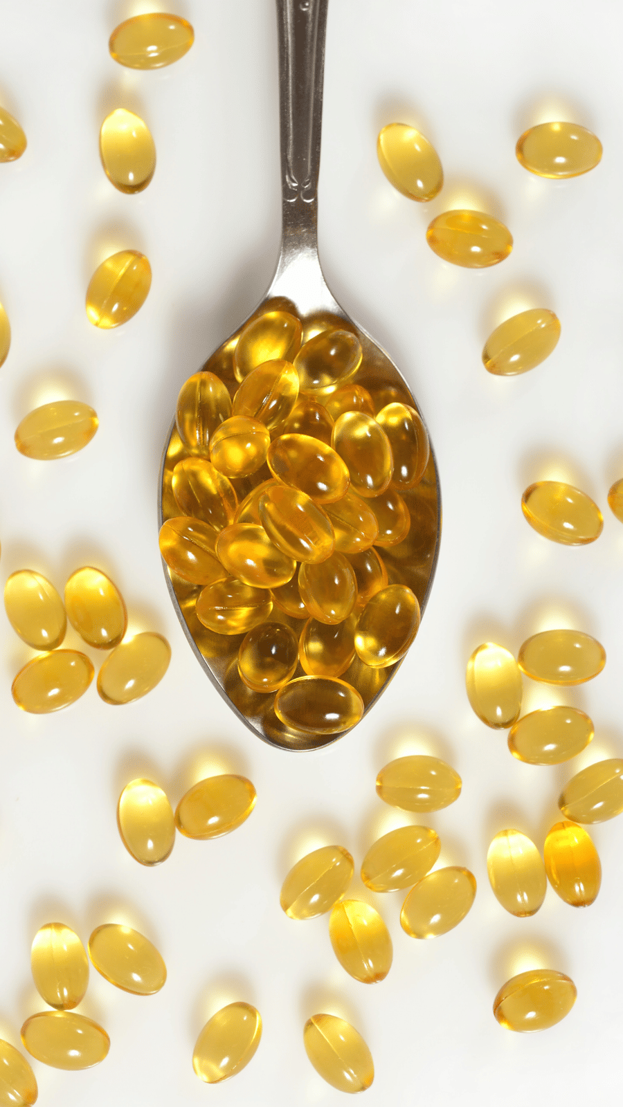 A metal spoon heaped with translucent softgel capsules, scattered across a flat surface