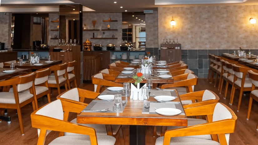 Well-arranged dining tables in Aromas restaurant at VITS Select, Bengaluru, with neat place settings and warm wooden interiors in full view.