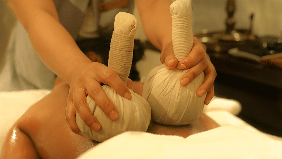 Traditional massage therapy at The Suryaa New Delhi featuring a therapist performing a spa treatment