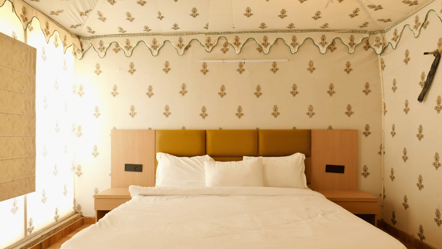 A tent-style hotel room at Grassfield Riviera Resort, with a large bed, patterned walls, and a wooden headboard.
