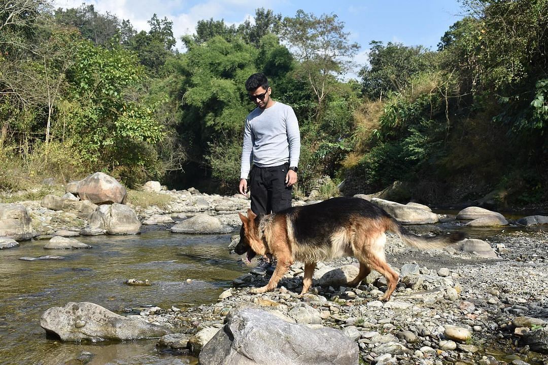A man with a dog standing on the edge of a stream at the Sylvan Retreat, Dehradun.