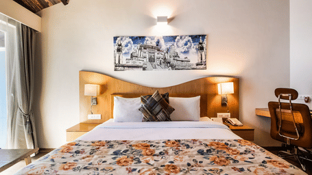 King-size bed with a wooden headboard, floral bedspread, wall art, and warm bedside lighting at Bamboo Saa Resort & Spa, Udaipur.