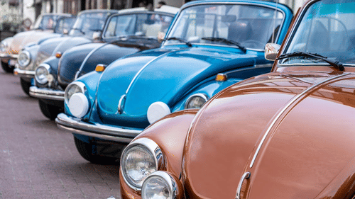 Classic vintage cars of different colours lined up in an outdoor setting.