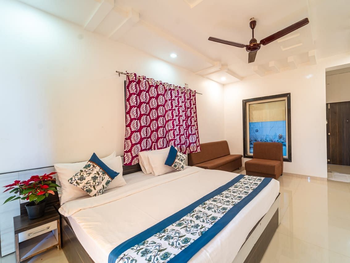 Deluxe Garden View Room showcasing the bed with blue and white linens, a decorative headboard, a patterned screen, a ceiling fan, and a glimpse into an adjacent area.