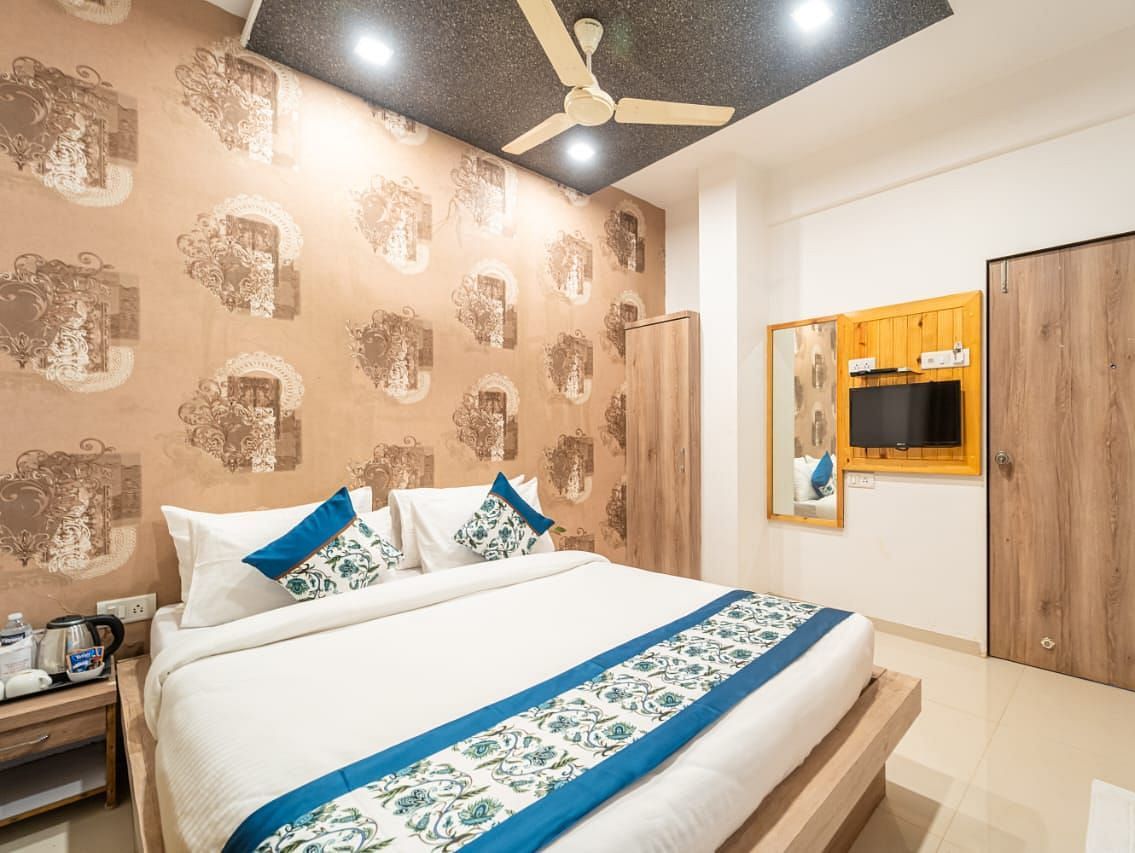 Standard Room featuring a bed with blue accents, patterned wallpaper, and a television.