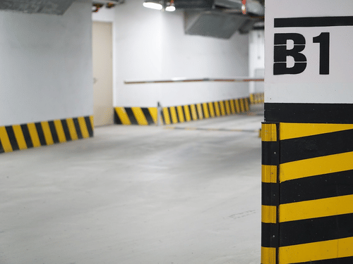An empty underground parking lot with a B1 labeled pillar and hazard stripes.