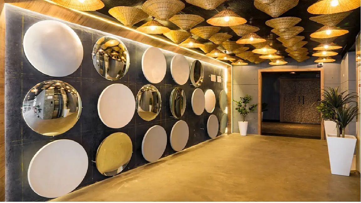A chic entrance hallway with reflective circular wall panels, warm ambient lighting, woven ceiling décor, and potted plants for a sophisticated welcome at TGI Livancia Hillside, JC Nagar, Mysore.