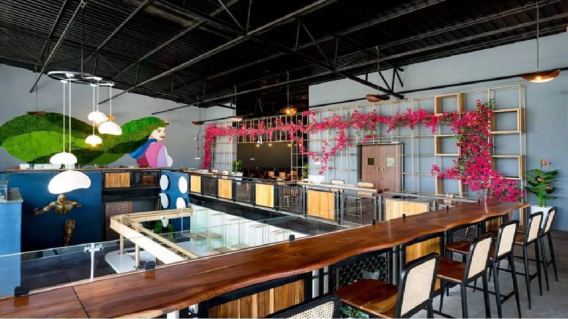A vibrant mezzanine-level dining area featuring a striking mural, lush green wall, floral accents, and a stylish bar with contemporary seating at TGI Livancia Hillside, JC Nagar, Mysore.