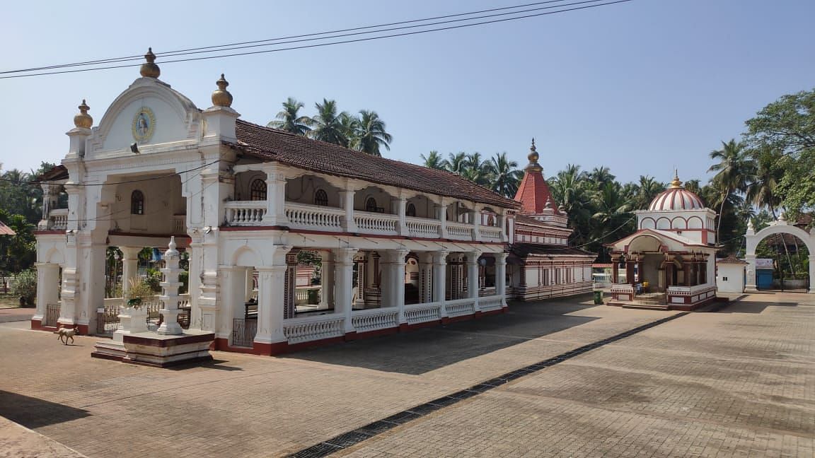 Ornate white temple with red tiled roof, balconies, arched windows, carvings and palm trees .