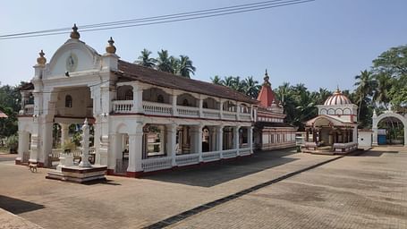 Ornate white temple with red tiled roof, balconies, arched windows, carvings and palm trees .
