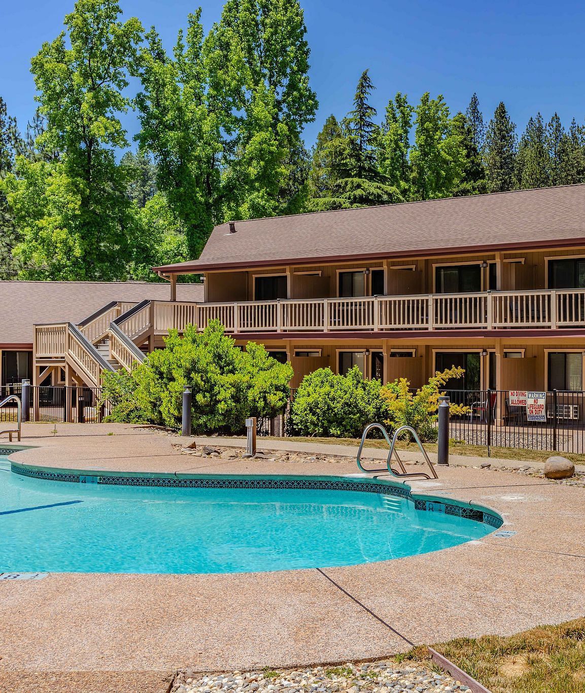 A view of an outdoor swimming pool with the hotel building in the backdrop on a clear, blue day - Amador Hotel.