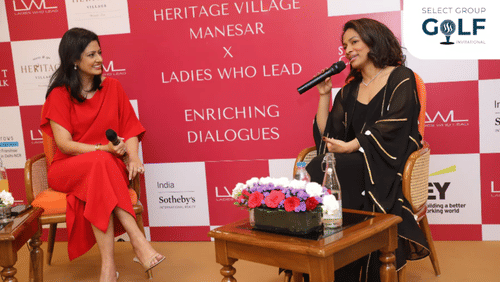 Two women speaking at Heritage Village event with microphones and flowers on the table