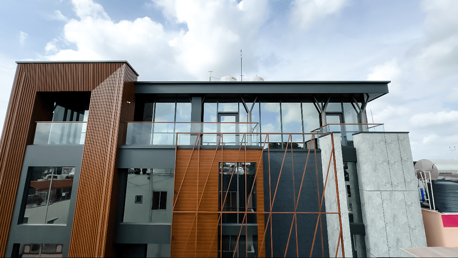 The exterior view of the building featuring a terrace proptected with glass hand rails at F Hotels, Bengaluru, with a cloudy blue sky in the bcakround.