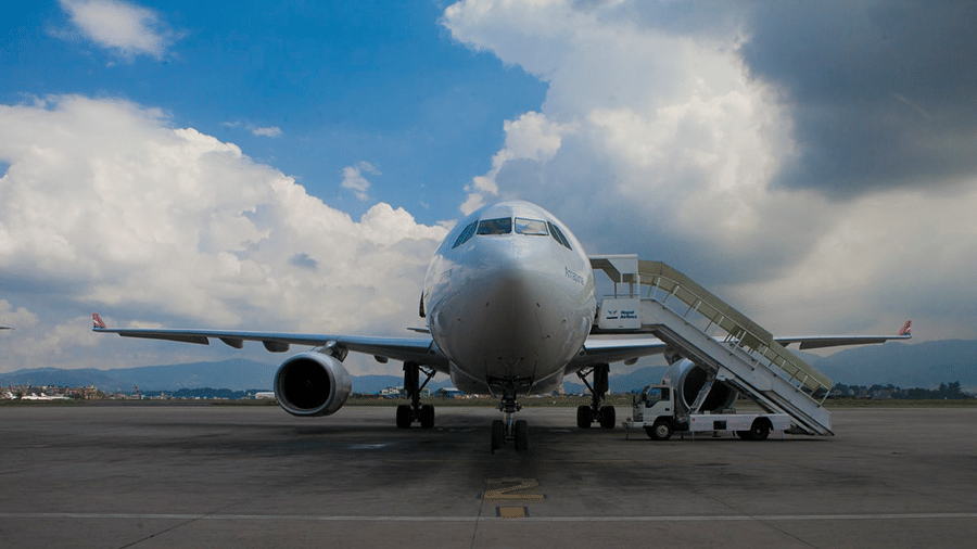Airplane parked on a tarmac with a staircase attached and clouds in the background.