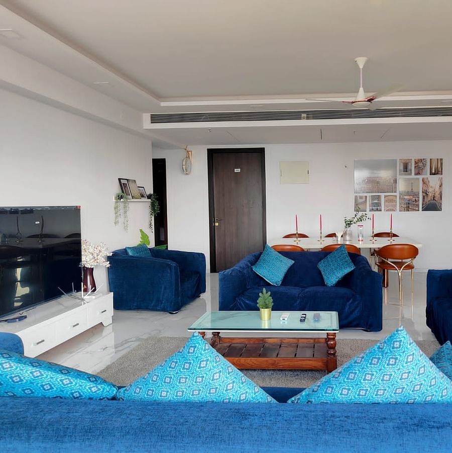3hall and living room area of Maxxvalue Hotel, Chitranjan Tower, Powai with blue themed couch and a dining table in the corner of the room