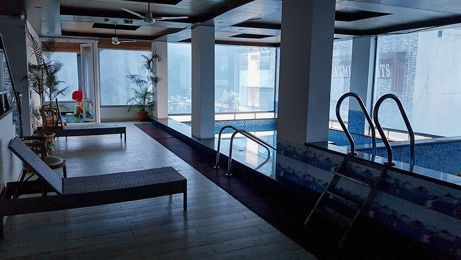 A dimly lit indoor swimming pool area with sun loungers kept besides it DLS Hotels On The Ganges.