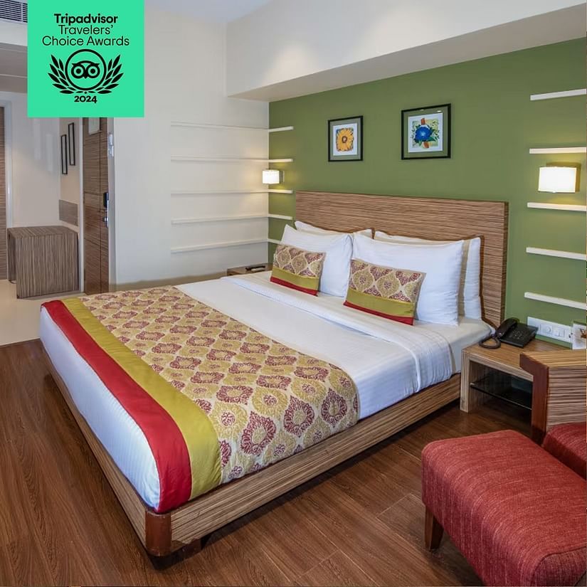 A stylish hotel room with a double bed, green accent wall, wooden flooring, and modern decor. Tripadvisor Travelers' Choice Awards 2024 badge displayed.