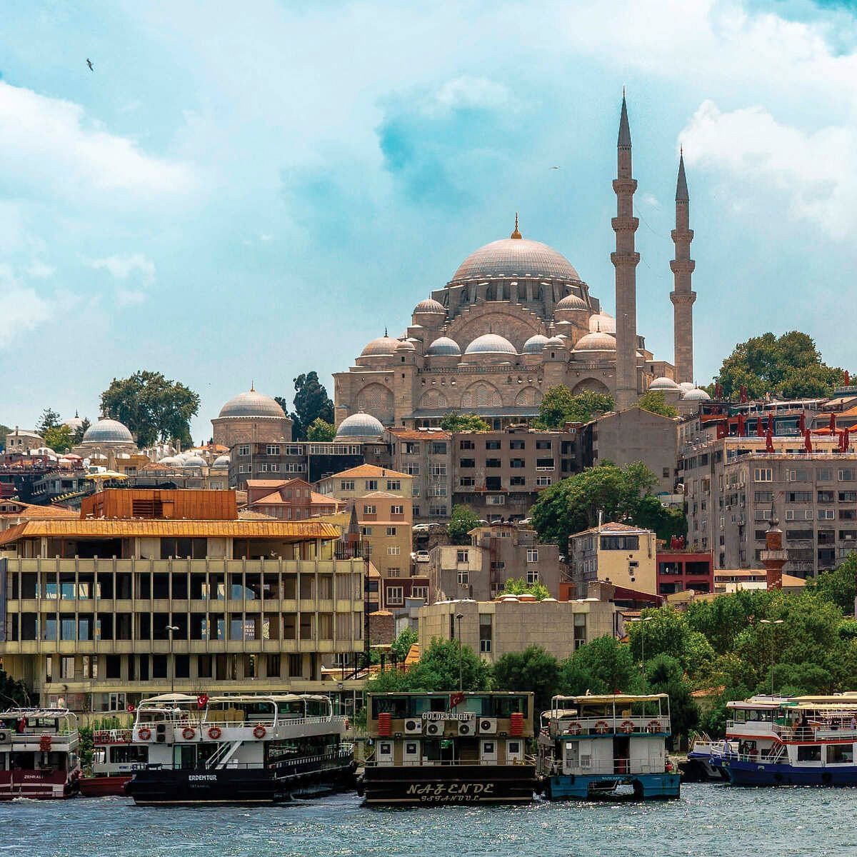 View of Istanbul waterfront with boats docked, lush greenery, and mosque minarets in the background.
