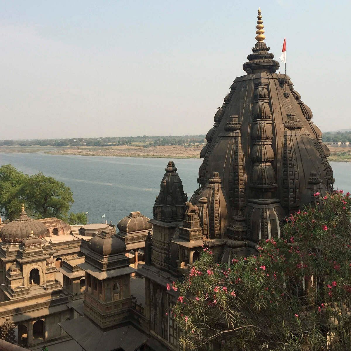 Stone temple overlooking a river, surrounded by smaller structures and greenery near the water.