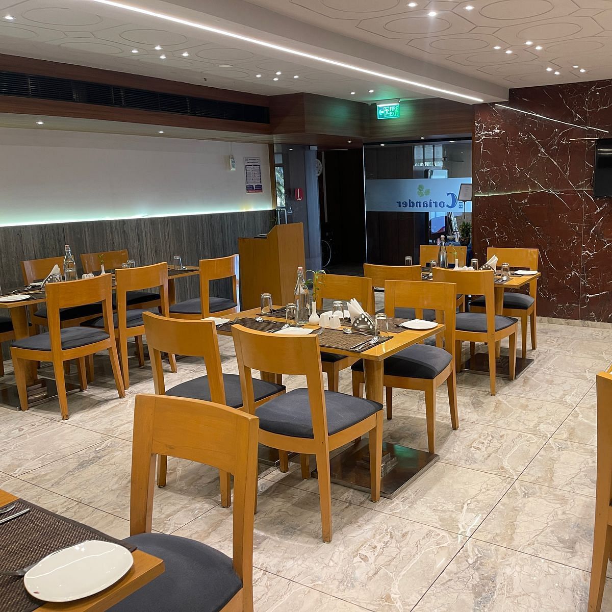 A modern indoor dining hall at the restaurant at Lords Eco Inn Dahej, featuring a T.V. on patterned red marbled wall at the background.