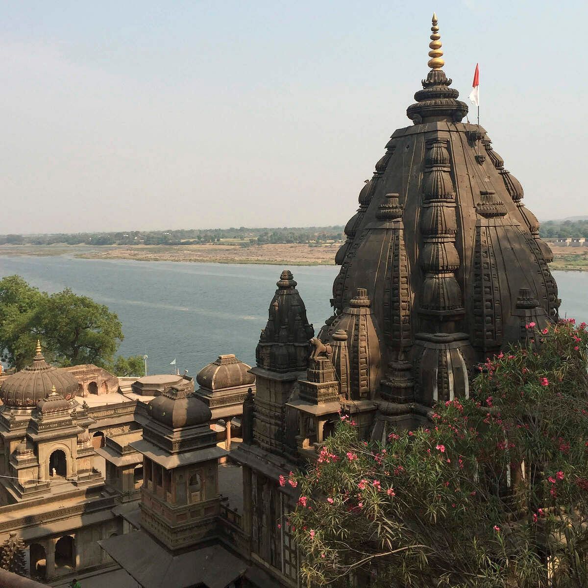 Stone temple overlooking a river, surrounded by smaller structures and greenery near the water.