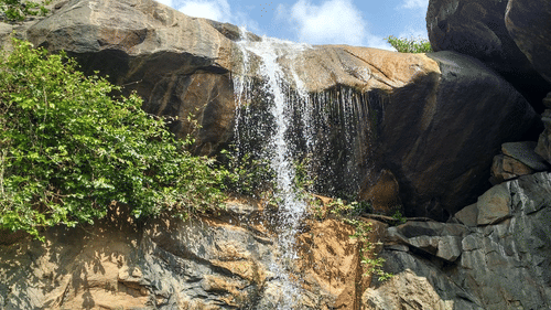 Waterfall flowing over large rocks surrounded by trees and greenery.