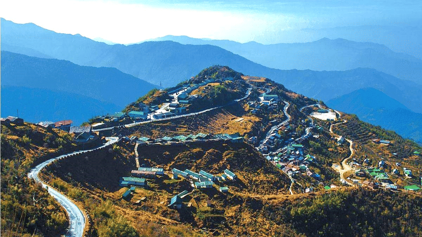Aerial view of Zuluk village nestled among the Himalayan hills in East Sikkim, with winding roads and layered blue mountain ranges in the background.