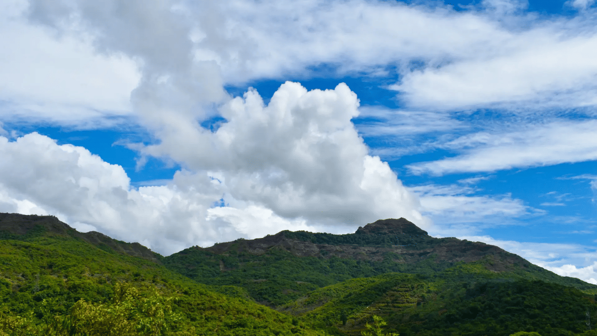 Cloud-filled sky over Coorg hills with lush green slopes, capturing the dramatic weather and scenic trekking terrain.