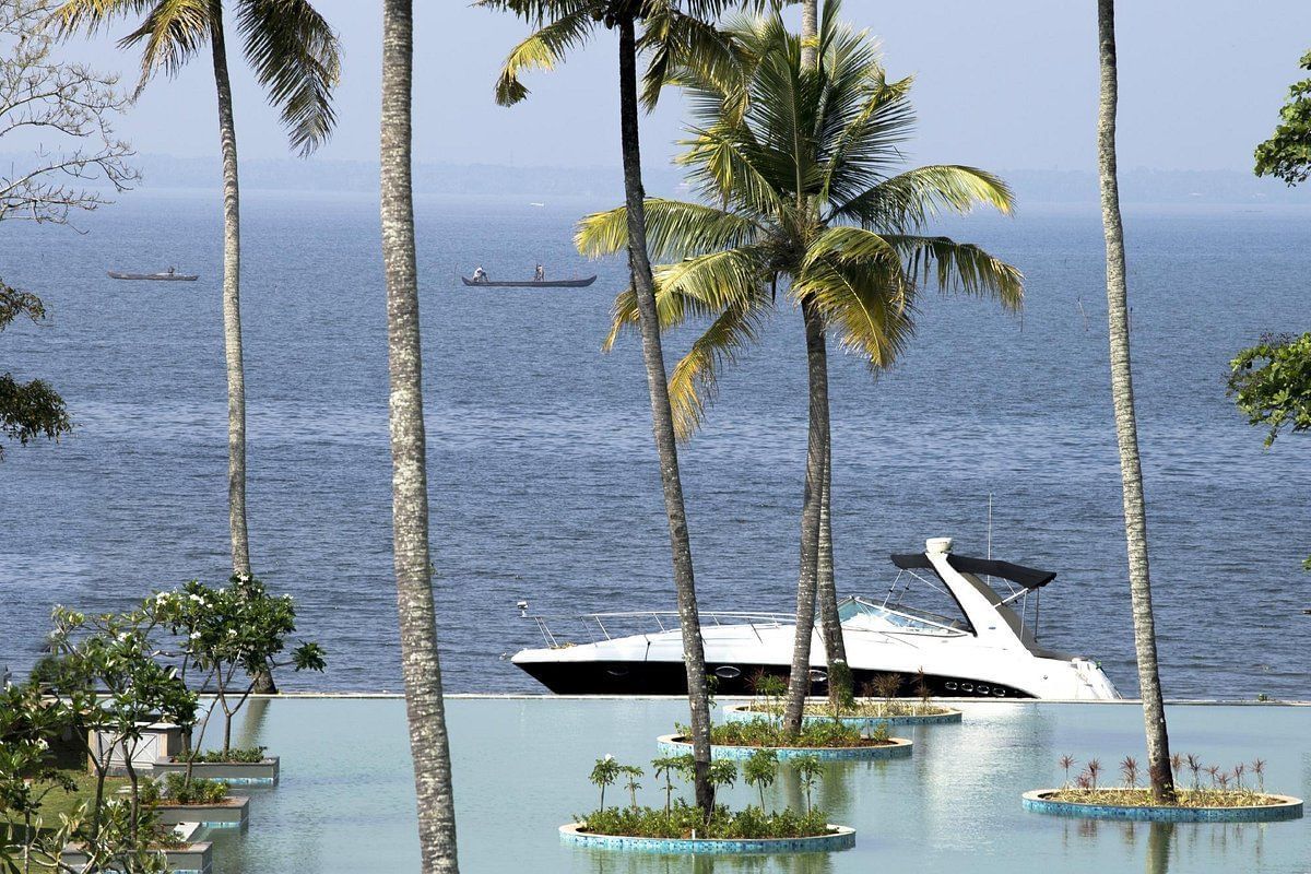 A boat gently floats on a Vembanad lake surrounded by coconut trees - Rhythm Kumarakom.